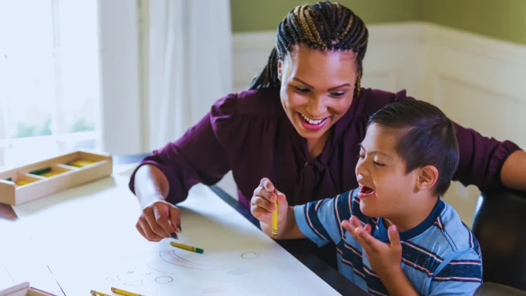 A home care professional drawing with a happy child with learning disabilities at a table