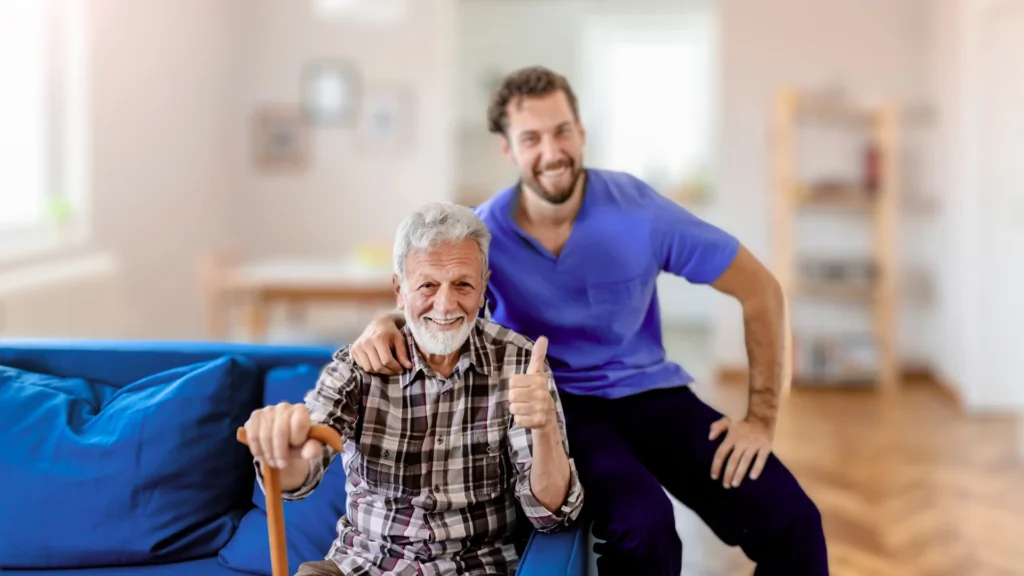 Smiling elderly man with caregiver offering home care support in a comfortable living space.