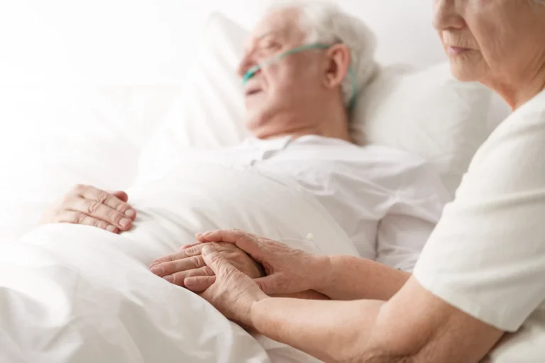 Wife holding her husband's hand who is receiving end-of-life care in Truro or Swindon.