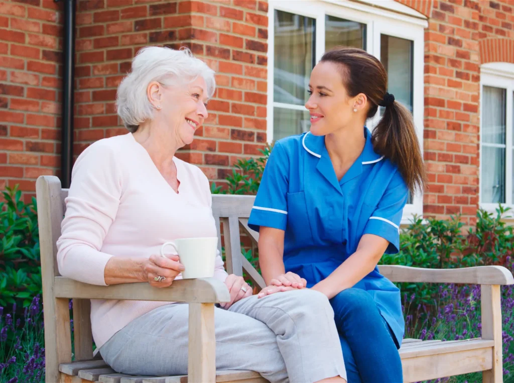 Elderly woman smiling while engaging in conversation with a caring home health nurse outdoors.