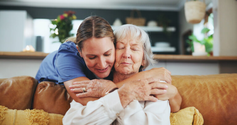 Smiling caregiver embracing elderly woman during respite care visit in Swindo