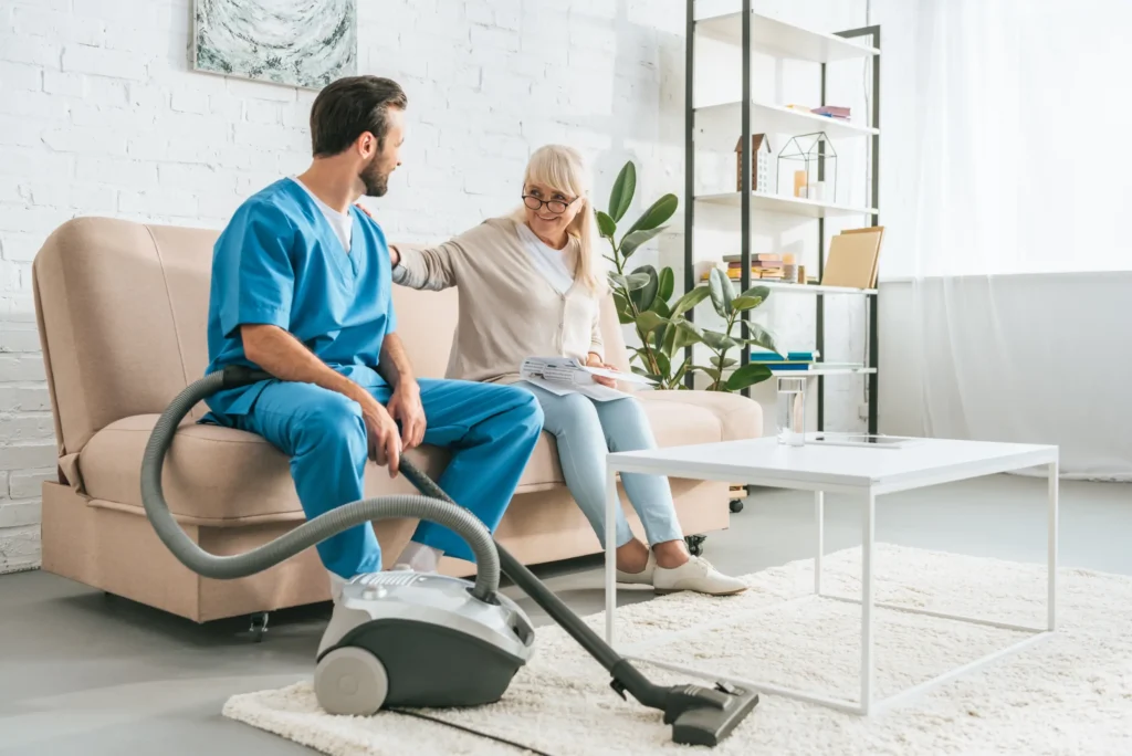 Carer assisting with light housekeeping while conversing with a senior woman on a couch in Truro or Swindon.
