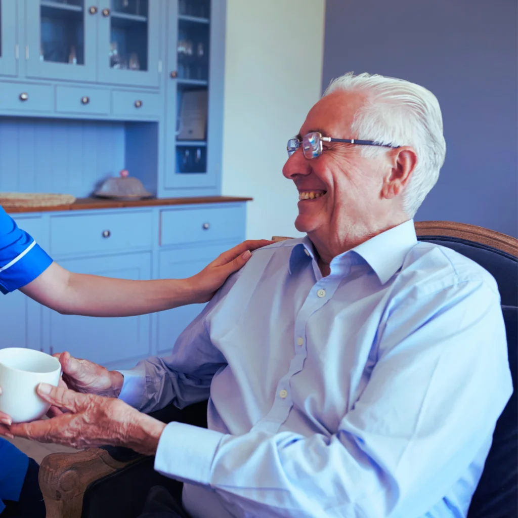 Carer smiling and pouring tea for an elderly person at home.