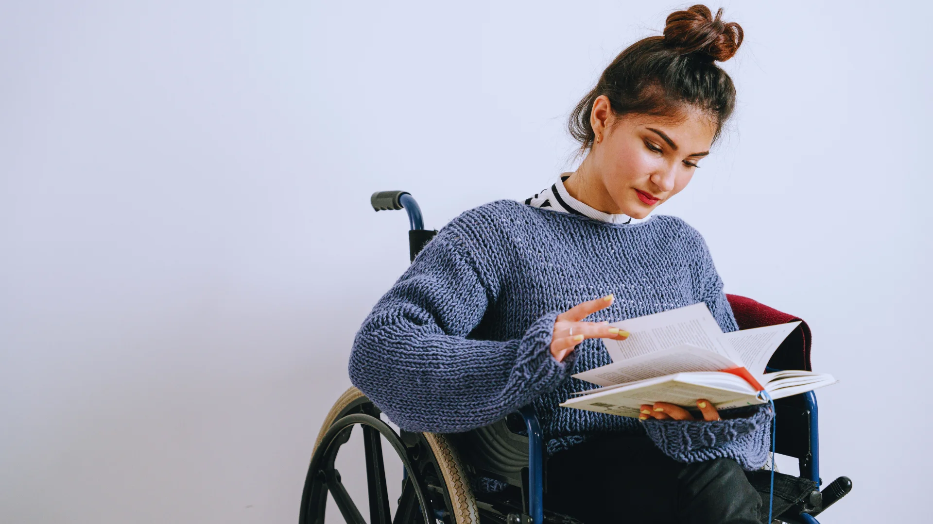 Young woman in a wheelchair reading a book at home.