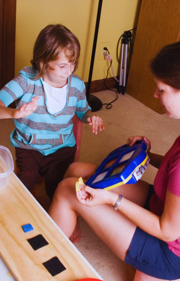 A carer supports an autistic child using communication aids and visual cards at home