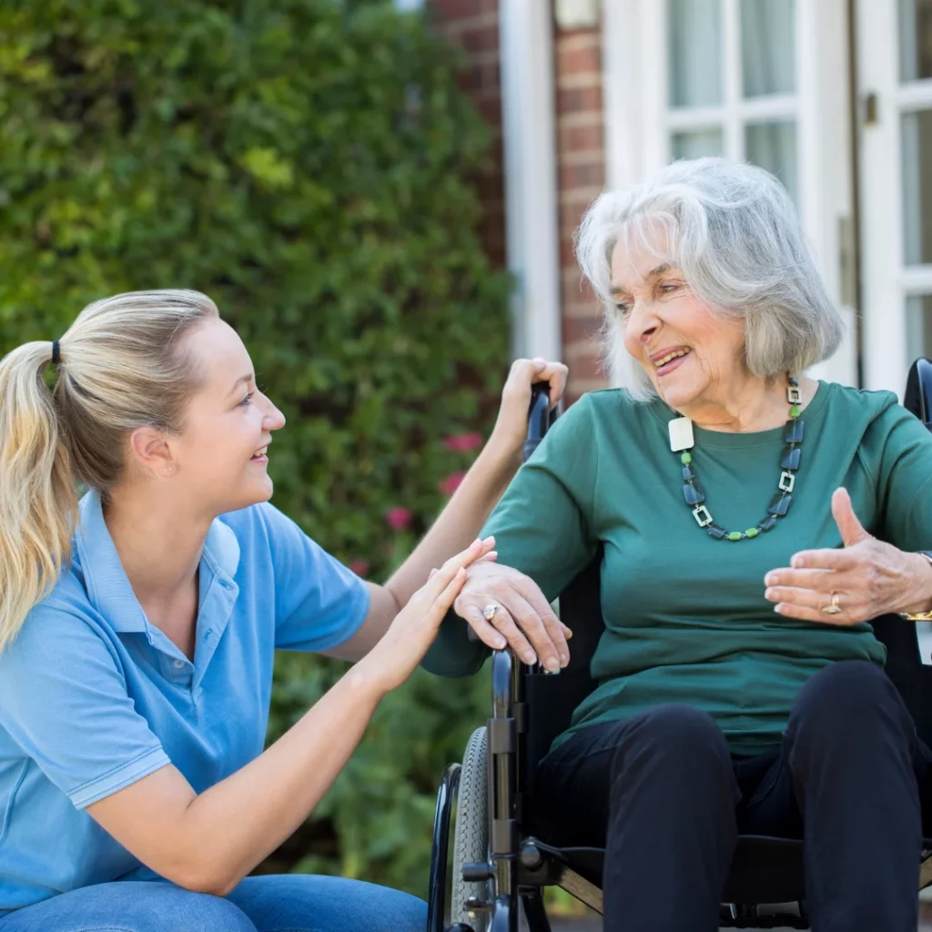 Smiling home carer chatting with an elderly woman in a wheelchair outside a home
